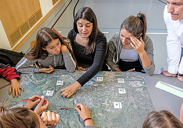Am Workshop: Schülerinnen beugen sich über das Luftbild von Dornach, interessiert beobachtet von
