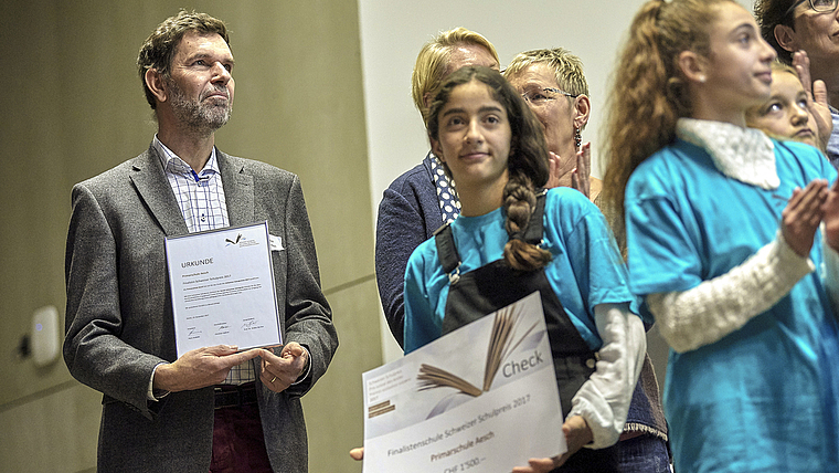 Eine Urkunde und 1500 Franken: Niggi Thurnherr, Schulleiter der Primarstufe Aesch, und eine Schülerin mit den verdienten «Trophäen» anlässlich der Verleihung des Schweizer Schulpreises am 13. Dezember in Bern. Foto: ZVG/Adrian Moser