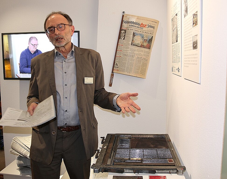 Zeitdokumente: Hanspeter Steiner, Leiter Ausstellung, präsentiert die Sonderzeitung, deren Frontseite nach altem Druckverfahren mit Bleisatz und Druckform hergestellt wurde. Auf dem Bildschirm im Hintergrund berichtet Thomas Immos über seine Zeit a