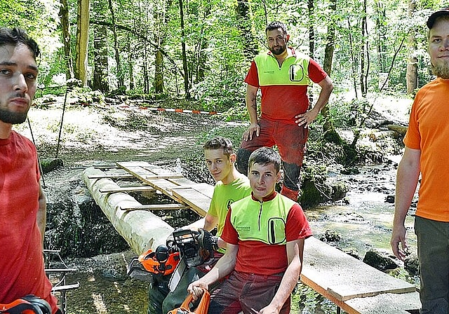 Kraftakt geschafft: Die beiden je eine Tonne schweren Tannen liegen als Brückenträger auf den Distanzhaltern der Wider- lager auf. Die Forstwarte in Ausbildung (v.l.) Janis, Nicola und Matthias, Kursinstruktor Stephan Erbsmehl und der Planer und an