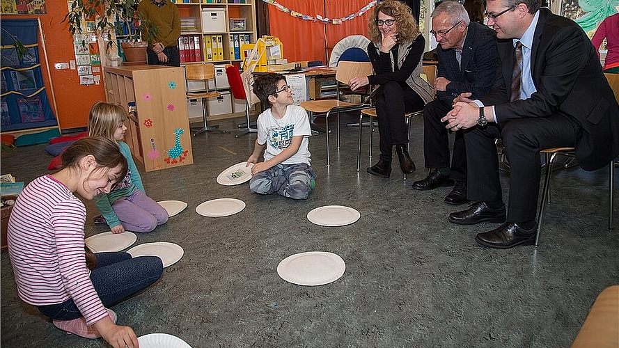 Kinder spielen Abfall-Memory: Die Gäste Bildungsdirektor Remo Ankli, Josef Christ, Esther Grond (v.r.) und Marco Maurer (im Hintergrund) schauen interessiert zu. Fotos: Martin Staub 
