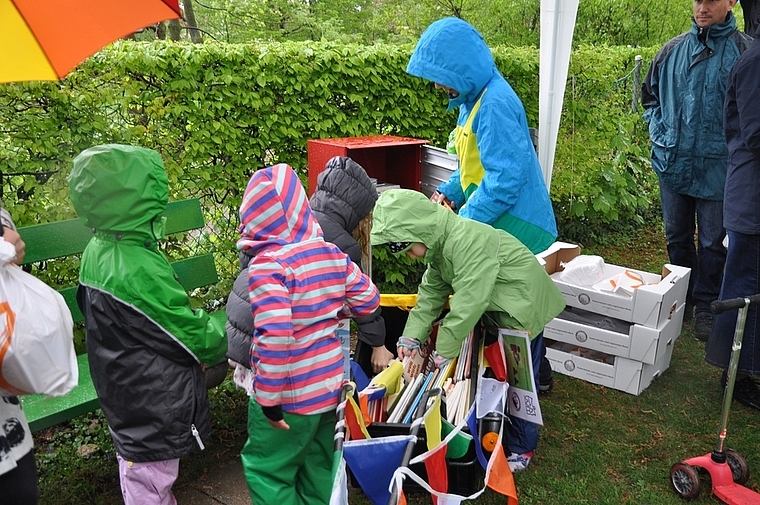 Trotz Regen eifrig dabei: Junge Leser befüllen einen Buchkasten des neu eröffneten Kinderbuchwegs in Münchenstein.