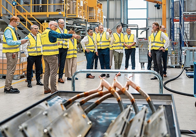 In der Industrieanlage in Büsserach: Ein Elantas-Mitarbeiter erläutert die Applikation der Primärisolierung auf Windkraft-Spulen. Foto: zVg/ Sandro Karrer