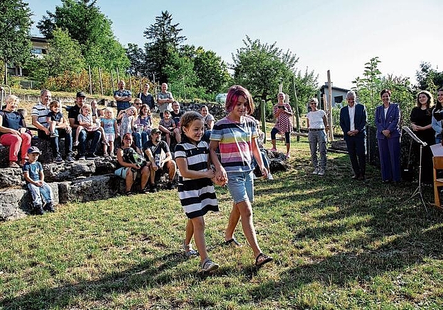 Aufnahme der Erstklässlerinnen und Erstklässler: Eine ältere Schülerin empfängt eine Erstklässlerin am ersten Schultag. Regierungsrätin Monica Gschwind (in violett) und Beat Lüthy, Leiter Amt für Volksschulen (weisses Hemd), sind Gäste in L