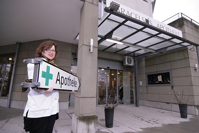 Wegweiser des Anstosses: Dieses Schild in den Händen von Paracelsus-Apothekerin Lisa Runyon wies jahrelang unbewilligt den Weg zu ihrer Apotheke – jetzt wird es von der Gemeinde Dornach nicht mehr geduldet. Foto: Lukas Hausendorf