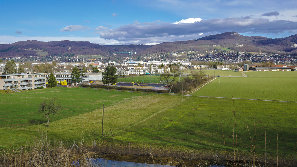 Hier plant der Kanton Baselland die Teilumfahrung Reinach: Von der Birsigtalstrasse herkommend, soll die neue Strasse um die Sportzone Fiechten (Bildmitte) führen und zwischen dem südlichen Siedlungsgebiet und Neuhof (Mittelgrund rechts) in die Hauptstrasse Reinach–Aesch münden. Foto: Edmondo Savoldelli
