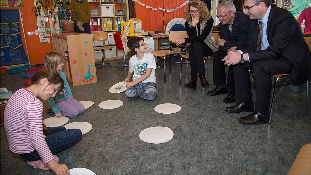 Kinder spielen Abfall-Memory: Die Gäste Bildungsdirektor Remo Ankli, Josef Christ, Esther Grond (v.r.) und Marco Maurer (im Hintergrund) schauen interessiert zu. Fotos: Martin Staub 
