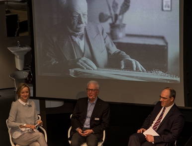 Podium: Giuseppe Gerster erzählt von seinen Erfahrungen mit der Keramik Laufen. Corinne Rüetschi, Moderatorin (l.), und CEO Klaus Schneider (r.). Im Hintergrund Firmen Mitbegründer Joseph Gerster-Roth. Foto: Martin Staub
